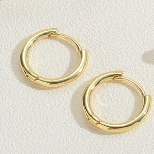 Close-up of 14K gold plated huggie earrings with polished mirror finish on textured background