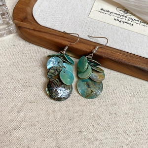 Détail de boucles d'oreilles pendantes en nacre d'abalone bleu-vert sur lin naturel