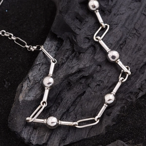 Minimalist silver chain necklace with metal beads on black charcoal background