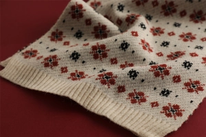 Close-up of beige knit scarf texture featuring red snowflake and flower patterns