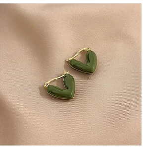 Close-up of heart-shaped olive green enamel hoop earrings on purple silk fabric