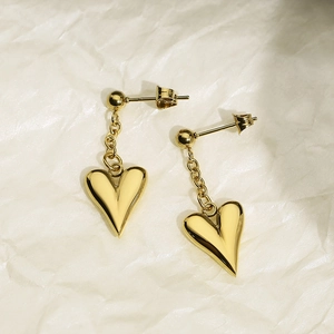 Close-up of elegant gold heart-shaped earrings with hanging chains on a textured background