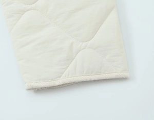 Close-up of diamond quilted fabric with woven piping detail on cream cotton jacket