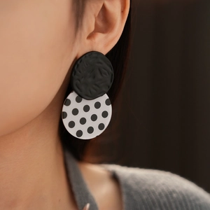 Close-up of black and white polka dot acrylic drop earrings worn by a fashion model