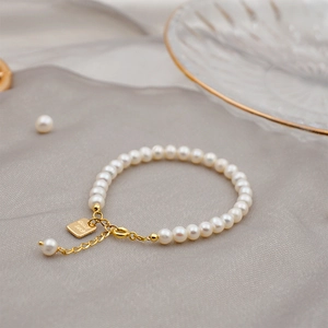 Elegant freshwater pearl bracelet with gold Good Luck charm on a textured grey background