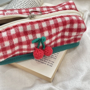 Detail of red checkered wool bag with crochet cherry charm on a vintage book