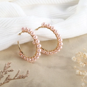 Detail of handmade gold hoop earrings with pink pearl beads on a neutral fabric background