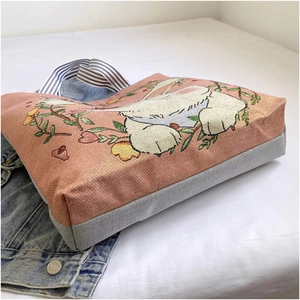 Detail of pink canvas tote bag with rabbit embroidery and striped handles on white bedding