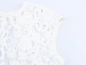 Détail macro de dentelle blanche et broderies florales sur l'épaule de la robe longue