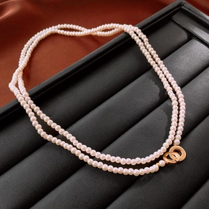 Detail view of double-layer pearl necklace with golden interlocking ring clasp on silk