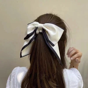Detailed back view of a large cream bow hair clip with black trim on long dark brown hair
