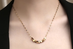 Close-up of minimalist gold chain necklace with small cube beads on model neck