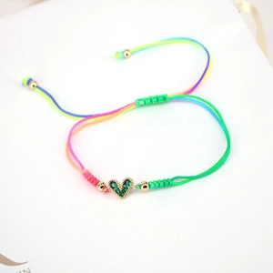 Detail of adjustable colorful braided bracelet with a heart-shaped green zircon charm
