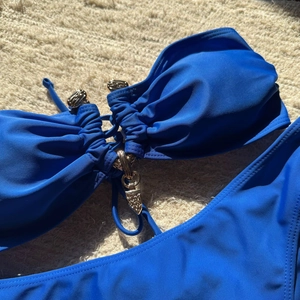 Détail d'un haut de bikini bandeau bleu avec pendentif en métal doré sur tissu