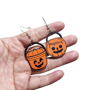 Dettaglio degli orecchini a zucca di Halloween in arancione e nero tenuti in mano