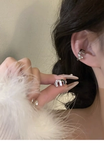 Macro detail of silver M-shaped ear cuff featuring zircon stones on a model's ear