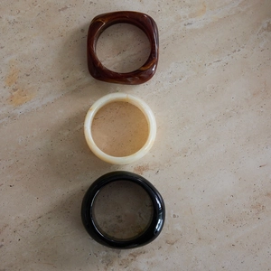 Dettaglio di bracciali in resina tartarugata, bianco crema e nero su marmo chiaro