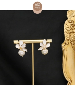 Detailed view of four-petal white flower earrings with zircon and pearls on a gold stand
