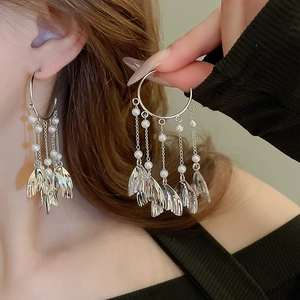 Metallic fishtail hoop earrings with long white pearl tassels and leaf charms on model