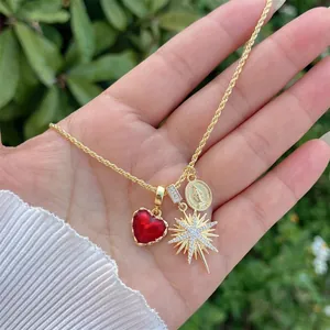 Detail of 18K gold-plated necklace featuring a red heart and star pendants on palm