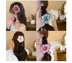 Close-up of large artificial flower hair clips in pink, blue, and gray on a model