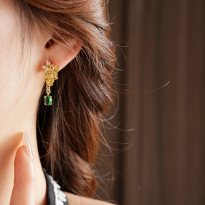 Détail de boucles d'oreilles fleurs dorées vintage avec pendentif gemme verte sur modèle