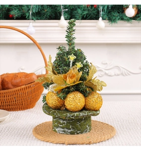 Close-up of mini Christmas tree with gold ornaments and snowflakes on a green base
