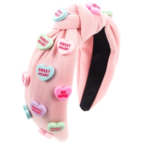 Détail d'un serre-tête rose noué avec des breloques en cœur macaron et texte doux