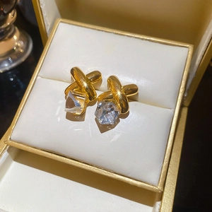 Detail showing gold crisscross earrings with faceted crystal in a premium jewelry box