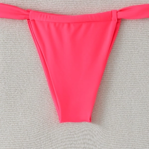 Detail of neon pink bikini bottom with high-cut design and side-tie knots on plush background