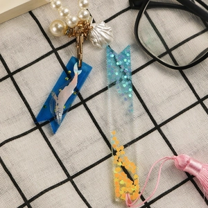 Detail of DIY epoxy resin bookmark with blue fish tail pendant and pink silky tassel