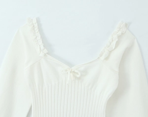 Close-up of white knit top featuring V-neckline with bow tie and ruffled shoulder straps