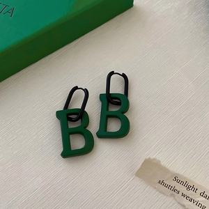 Detail view of retro green letter B earrings with black hoops on fabric background