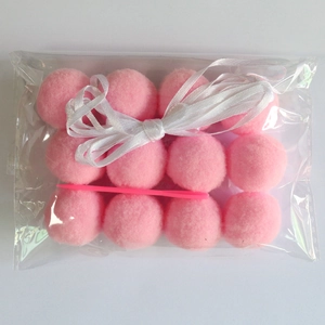 DIY kit featuring pink pom poms, white ribbon, and a plastic needle for party decorations