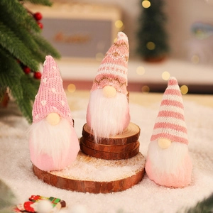 Close-up of three pink knitted Christmas gnomes on wooden base with warm holiday lights