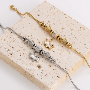 Gold and silver snake chain bracelets with unicorn shell pendants on stone surface