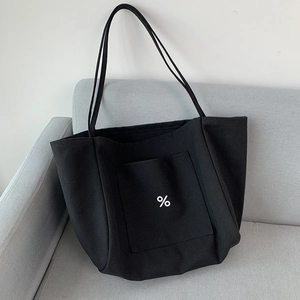 Detail of a black large-capacity canvas tote bag with a front pocket on a gray sofa