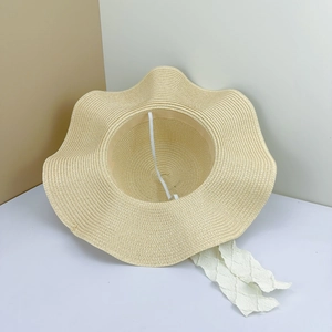 Detail of hand-woven straw hat featuring wavy edges and elegant white ribbon ties