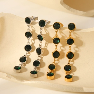 Detail of gold and silver drop earrings with emerald green gemstones on stone base