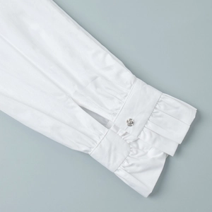 Detail view of white long sleeve shirt cuff with silver button and elegant ruffle pleats