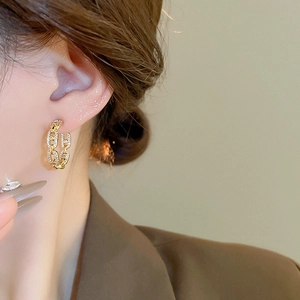 Detail of C-shaped gold chain earrings with sparkling zircons worn by a female model