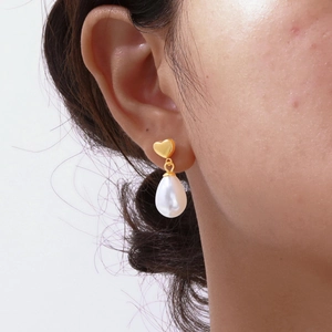 Close-up of heart-shaped gold stud with drop pearl earring worn on model's ear