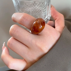 Detail of amber resin oval ring styled with a brown blazer for a vintage aesthetic look