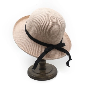 Detail of beige straw sun hat featuring a black satin ribbon bow on a wooden stand