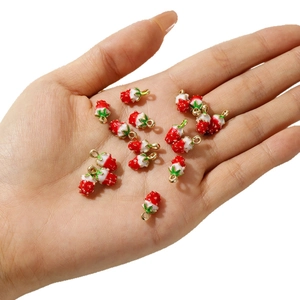 Handheld view of red and white alloy strawberry charms for DIY jewelry making