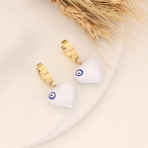 Detailed close-up of golden heart evil eye earrings with white enamel on a white tray
