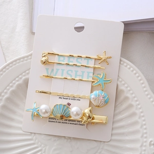 Golden starfish and shell hair clip set with blue enamel and pearls on display card