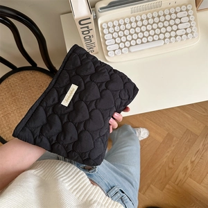 Quilted heart-patterned black makeup pouch held by hand in a cozy lifestyle setting