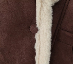 Détail d'une veste en daim marron avec bordure en laine de mouton blanche et bouton assorti
