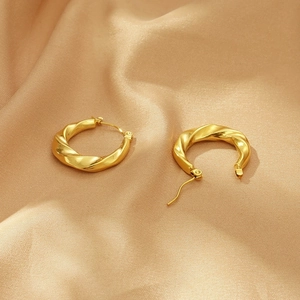 Close-up of twisted golden hoop earrings displayed on soft silk fabric background